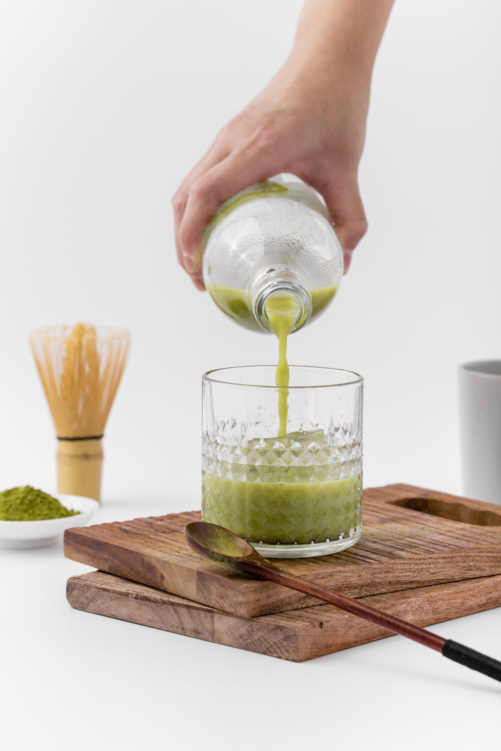 close up hand pouring matcha tea into glass